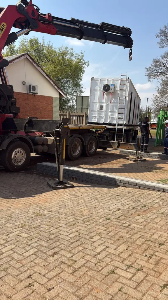 Crane truck delivering an air-conditioned container unit to site